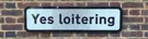 A street sign on a brick wall: Yes loitering